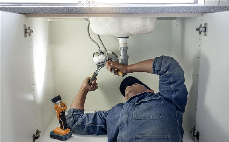 Plumber repairing pipes beneath a bathroom sink in Los Angeles